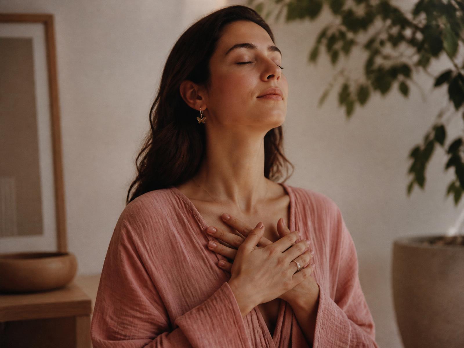 Woman in dusty rose linen with hands on her chest, eyes closed, softly lit — nervous system regulation and Vata balance